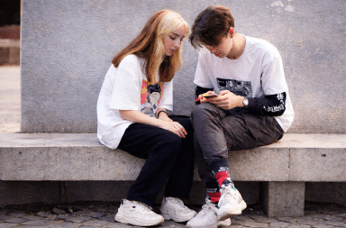 Deux adolescents assis côte à côte consultent un smartphone, illustrant l’usage des réseaux sociaux et son impact sur l’attention des jeunes.