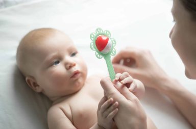 Un nourrisson éveillé, allongé sur le dos, observant attentivement un hochet avec un regard concentré.