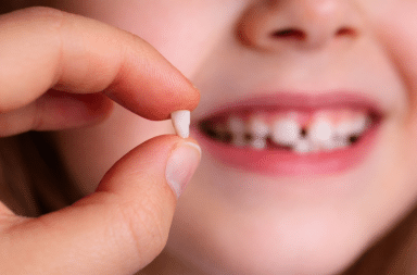 main tenant une dent de lait devant le sourire d’un enfant