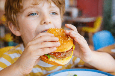 enfant mange un hamburger illustrant les effets de la malbouffe durant l’enfance