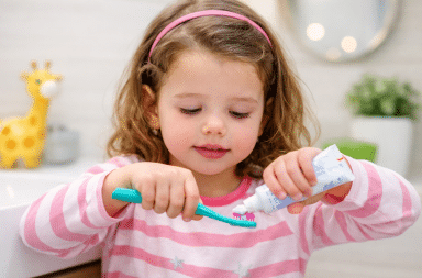 petite fille met du dentifrice sur sa brosse à dents avant de se brosser les dents